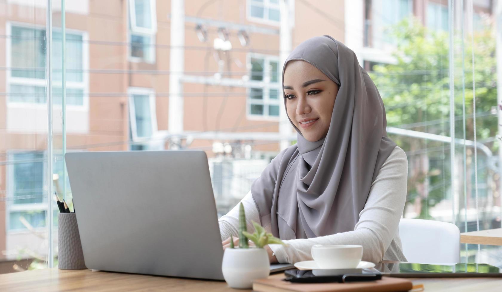 mulher de negócios muçulmana asiática no lenço hijab trabalhando com computador portátil no escritório moderno. pessoas de negócios, diversidade e conceito de escritório foto