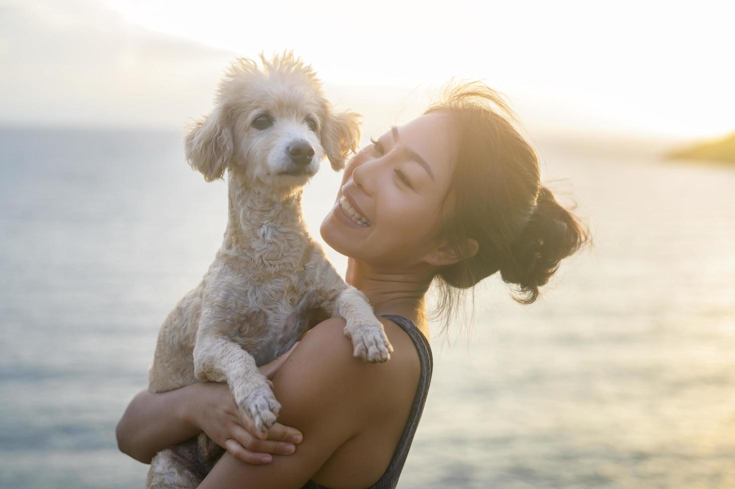 jovem mulher bonita com seu cachorro curtindo e relaxando à beira-mar durante o pôr do sol, verão, férias, feriados, conceito de estilos de vida. foto