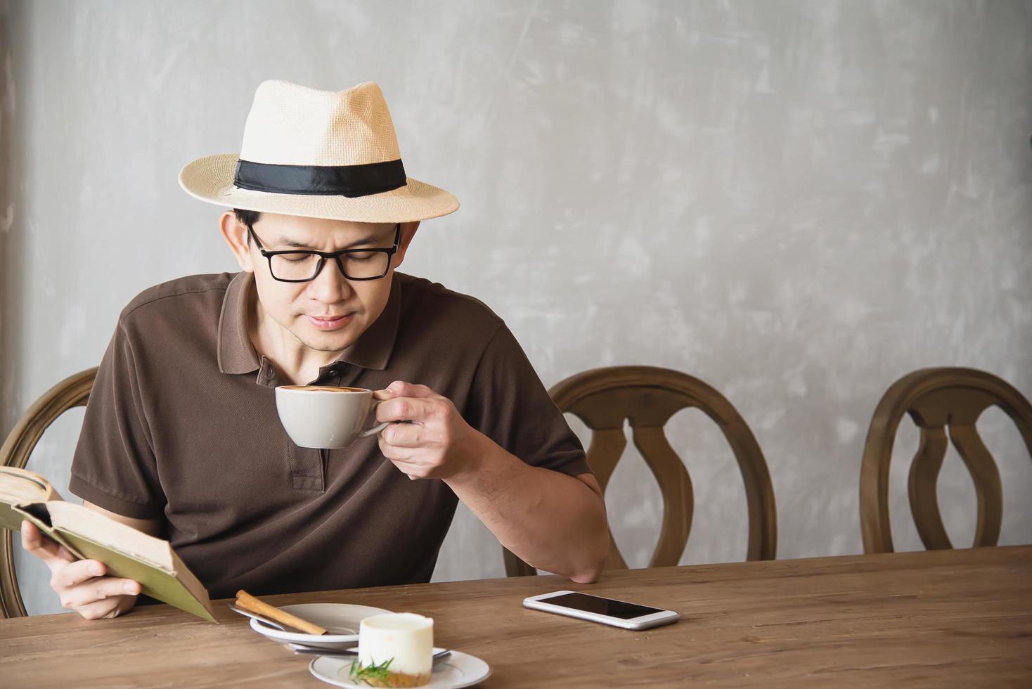 relaxe o homem asiático beba café e leia o livro em uma cafeteria de estilo moderno - pessoas com conceito de estilo de vida fácil de xícara de café foto