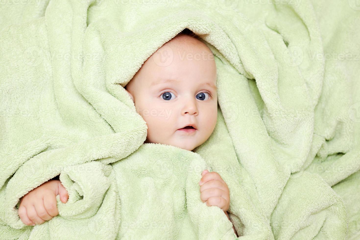 menino caucasiano coberto com toalha verde sorri com alegria foto