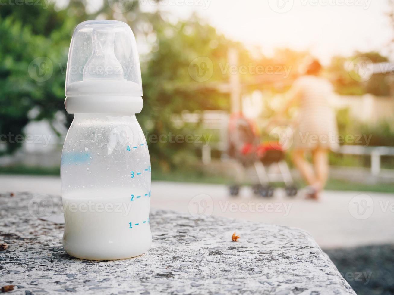 garrafa de leite de bebê na mesa de pedra sobre a mãe com fundo de carrinho de bebê foto