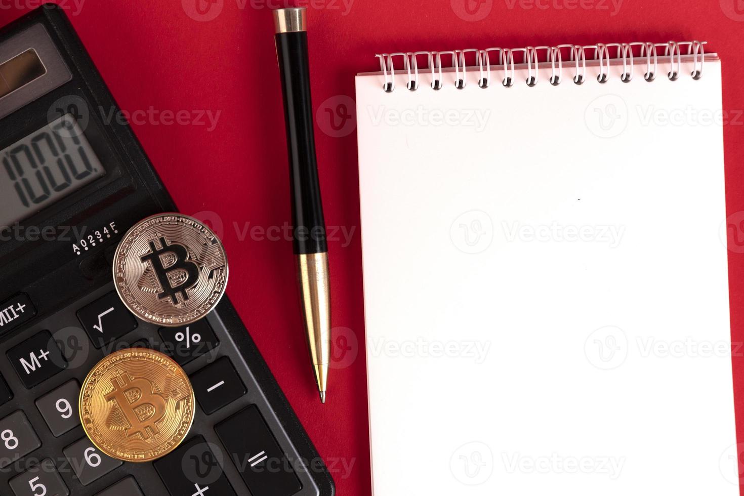 bloco de notas branco com calculadora, caneta elegante e moedas de bitcoin em um fundo vermelho. copie o espaço. foto