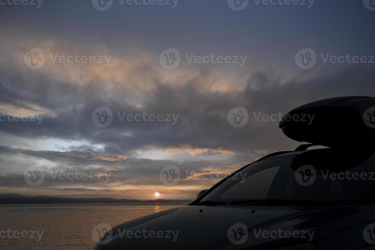 um carro com um porta-malas com uma caixa de carga, no contexto do nascer do sol sobre o mar. foto