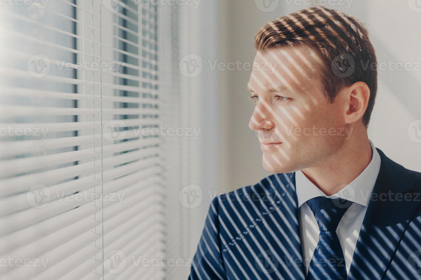 pessoas e conceito de carreira. jovem empresário de terno rico, pensa no futuro de sua empresa, fica perto da janela do escritório, concentrou um olhar pensativo. diretor administrativo masculino interno no gabinete foto