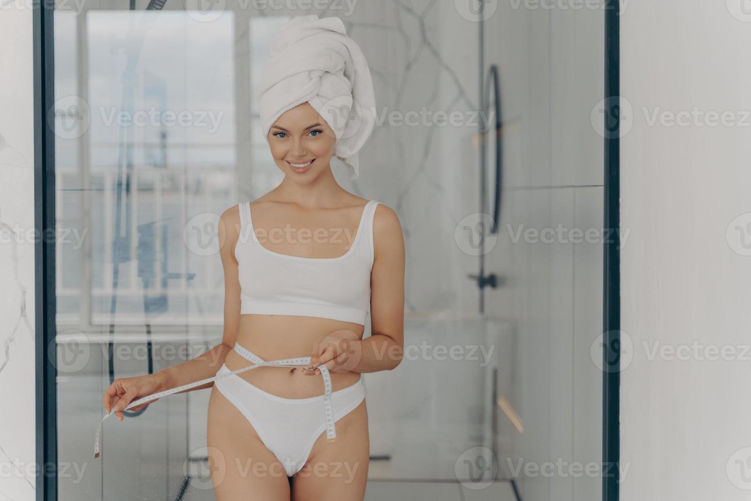 garota de ajuste positivo feliz posando no banheiro após o banho matinal com fita métrica segurando em volta da cintura foto