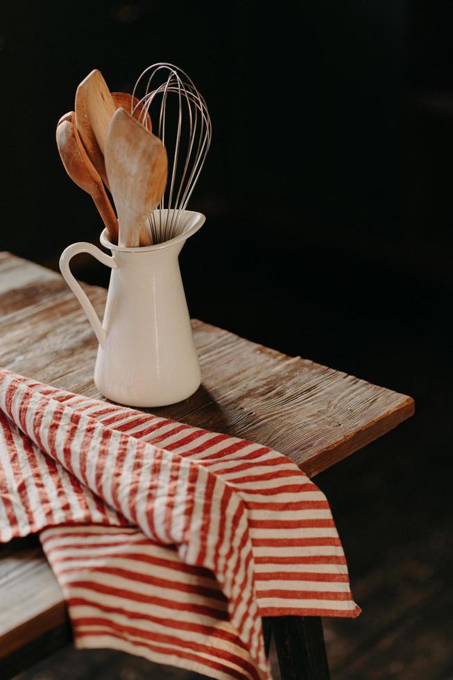 tiro vertical de utensílios de cozinha vintage em pote de cerâmica branca na mesa de madeira. decoração de cozinha em casa. utensílios de cozinha para cozinhar. coisas de casa foto