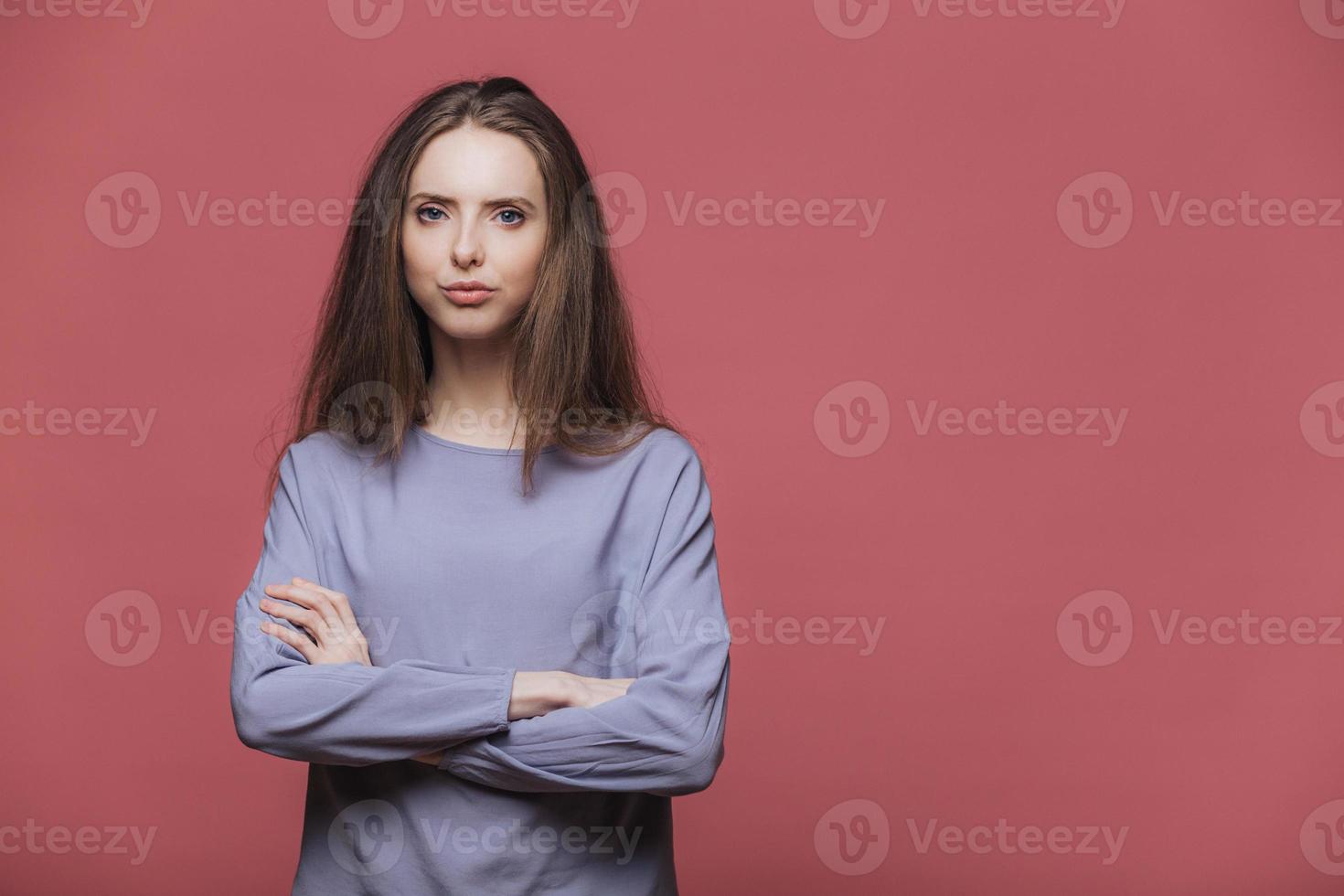 modelo feminino atraente sério confiante mantém as mãos cruzadas, usa roupas casuais, ouve atentamente as informações, posa contra um fundo rosa com espaço de cópia em branco para o seu texto promocional foto