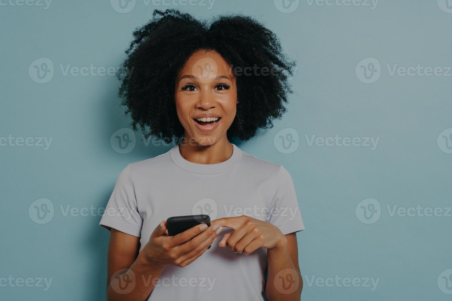 linda garota de pele escura feliz segurando smartphone moderno e conversando com um amigo online foto
