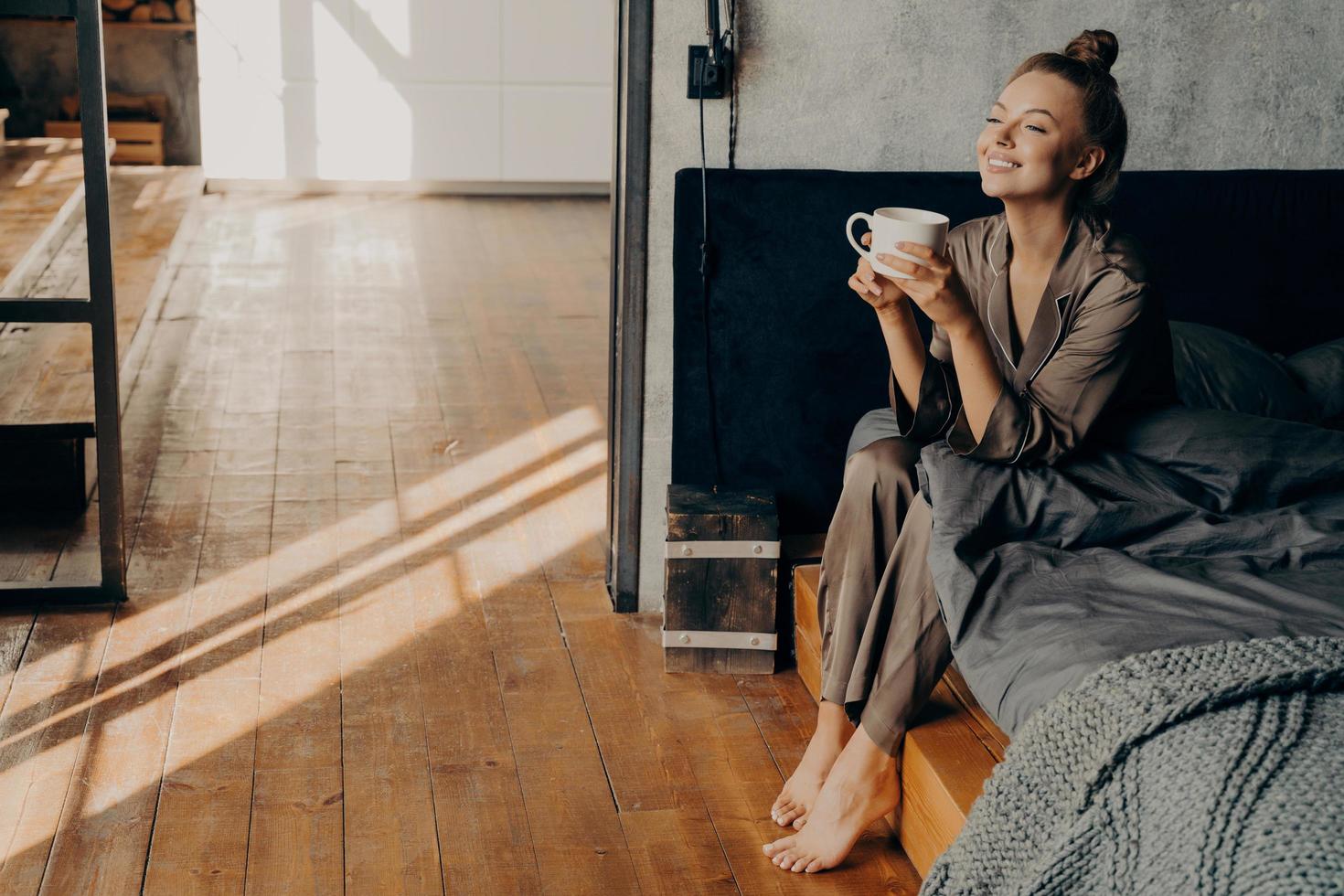linda garota bonita com uma xícara de café da manhã relaxando enquanto está sentado na cama foto