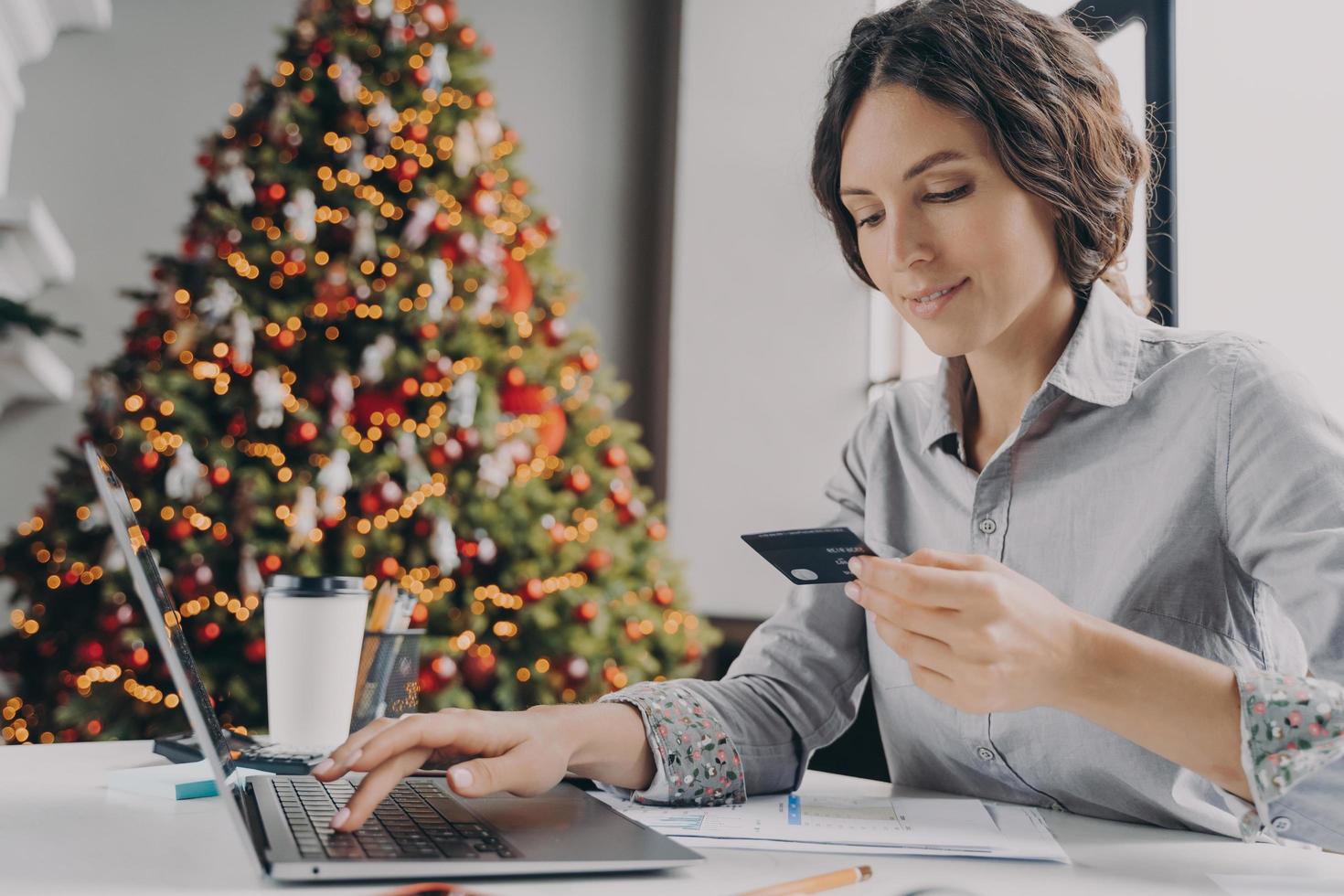 compras on-line de natal, jovem italiana segurando cartão de crédito plástico e digitando no laptop foto