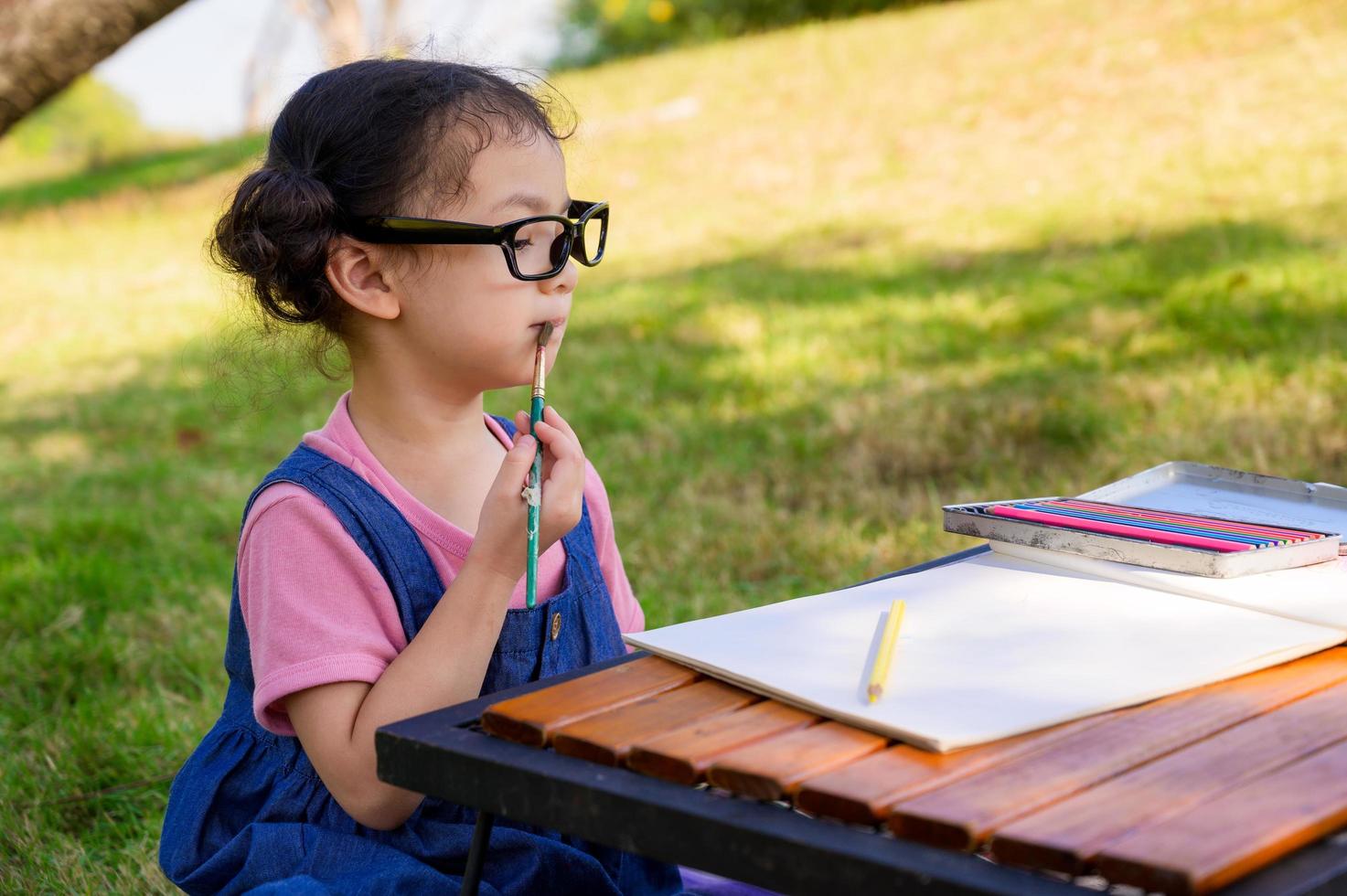 uma garotinha está sentada no pano e se prepara pintada no papel colocado em uma mesa foto