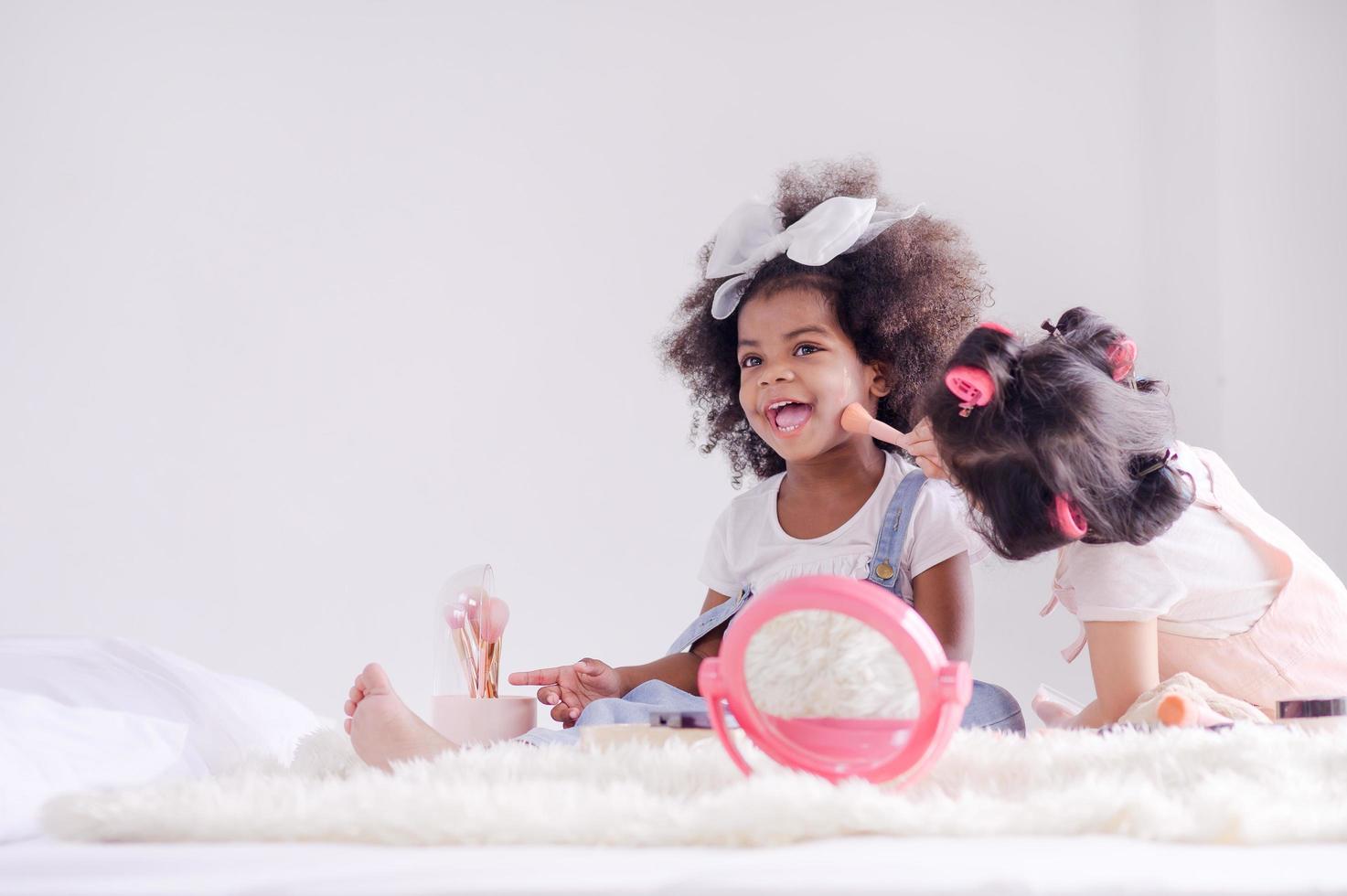 uma menina asiática bonitinha e um amigo africano estão alegremente aplicando pincéis de maquiagem com pó em seu quarto foto