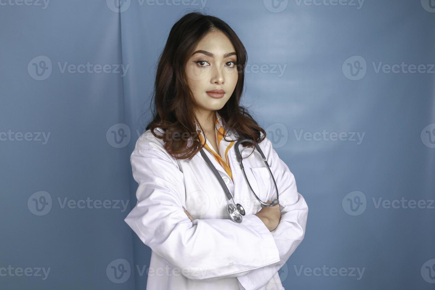 retrato de uma médica confiante atraente, braços sorridentes amigáveis cruzados usam estetoscópio de jaleco branco isolado fundo de cor azul foto