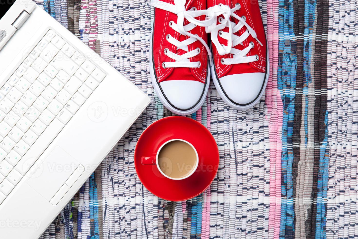 xícara de cappuccino perto de sapatos desportivos vermelhos e computador foto