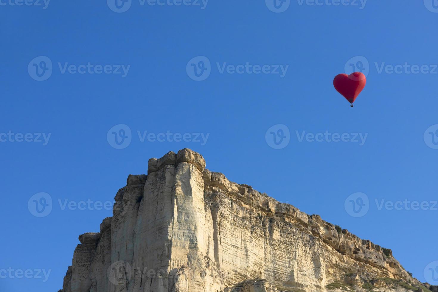 balão de ar quente, balão vermelho em forma de coração voador no contexto da rocha branca. foto