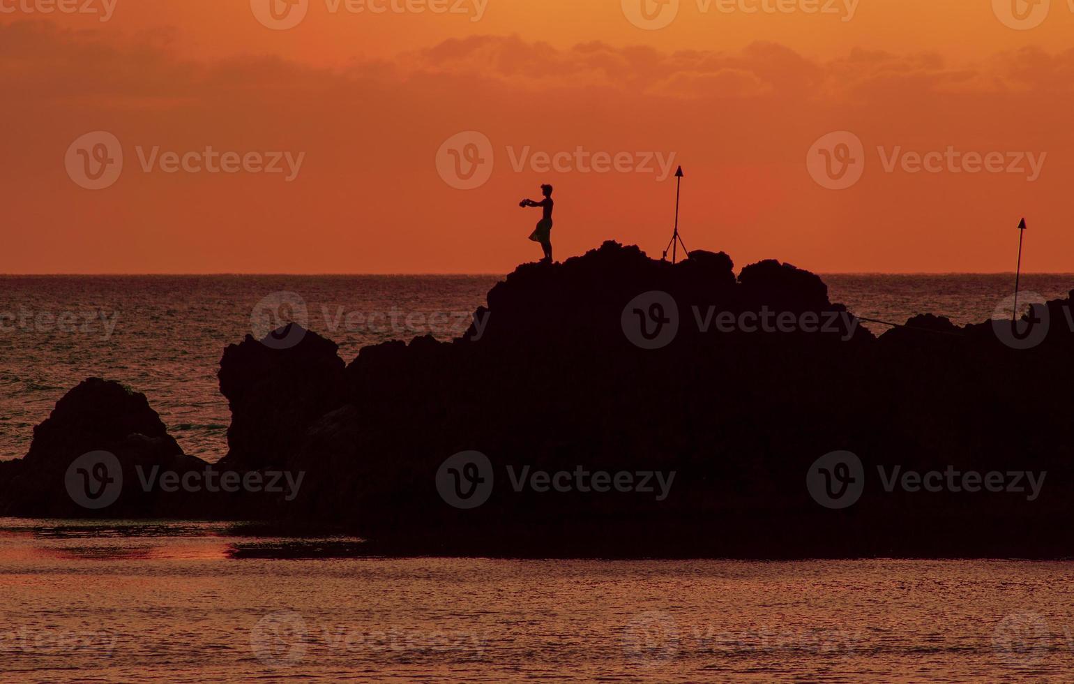 mergulhador de penhasco havaiano contra um pôr do sol laranja foto