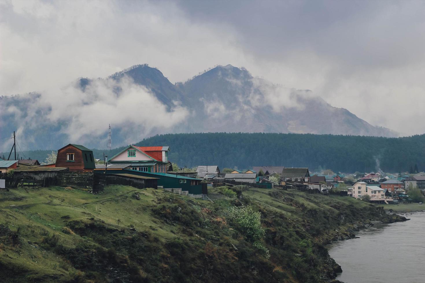 aldeia perto do rio na montanha arborizada de fundo em nevoeiro e nuvem. bela paisagem com floresta de abetos em denso nevoeiro foto