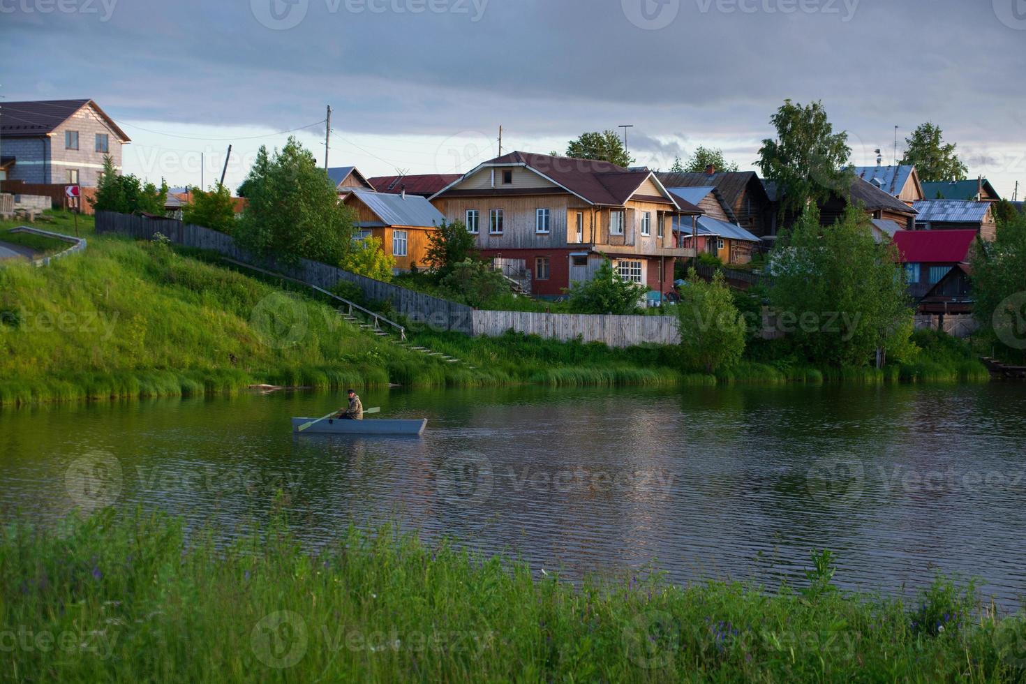 uma vila na margem do rio com grama verde brilhante e um lindo céu. foto