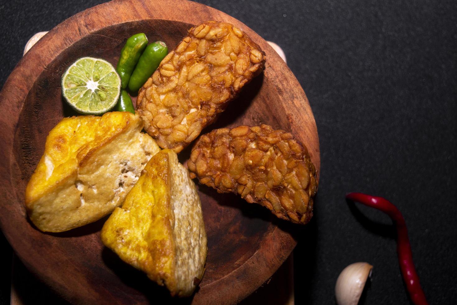 comida indonésia. tofu, tempeh, limão, alho e pimenta em fundo preto. foto