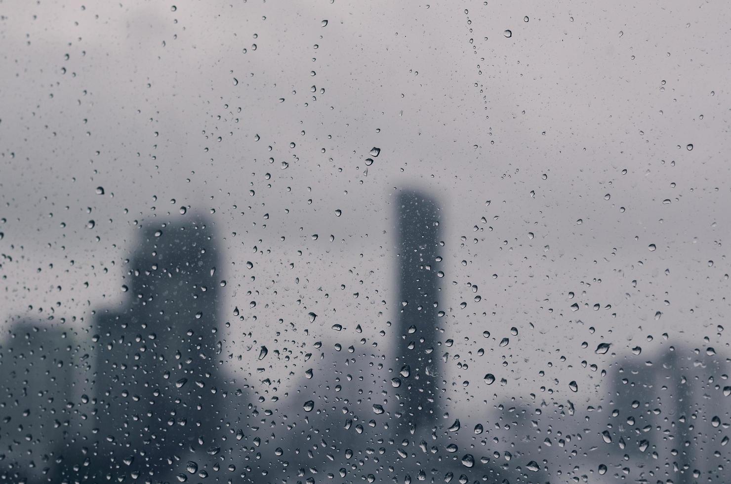 gota de chuva na janela de vidro na estação das monções com fundo desfocado de edifícios da cidade. foto