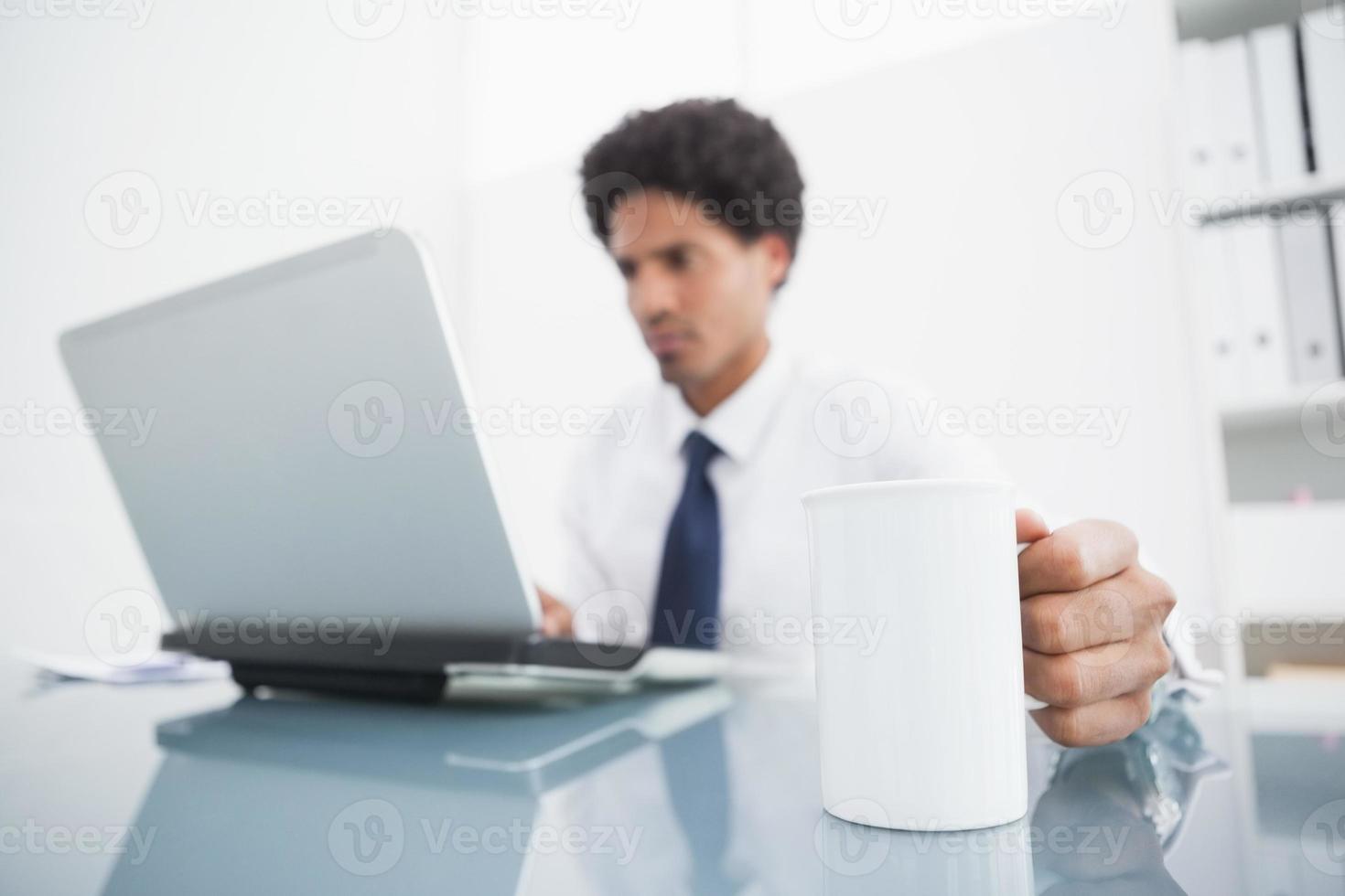 empresário usando laptop e segurando a caneca na mesa foto