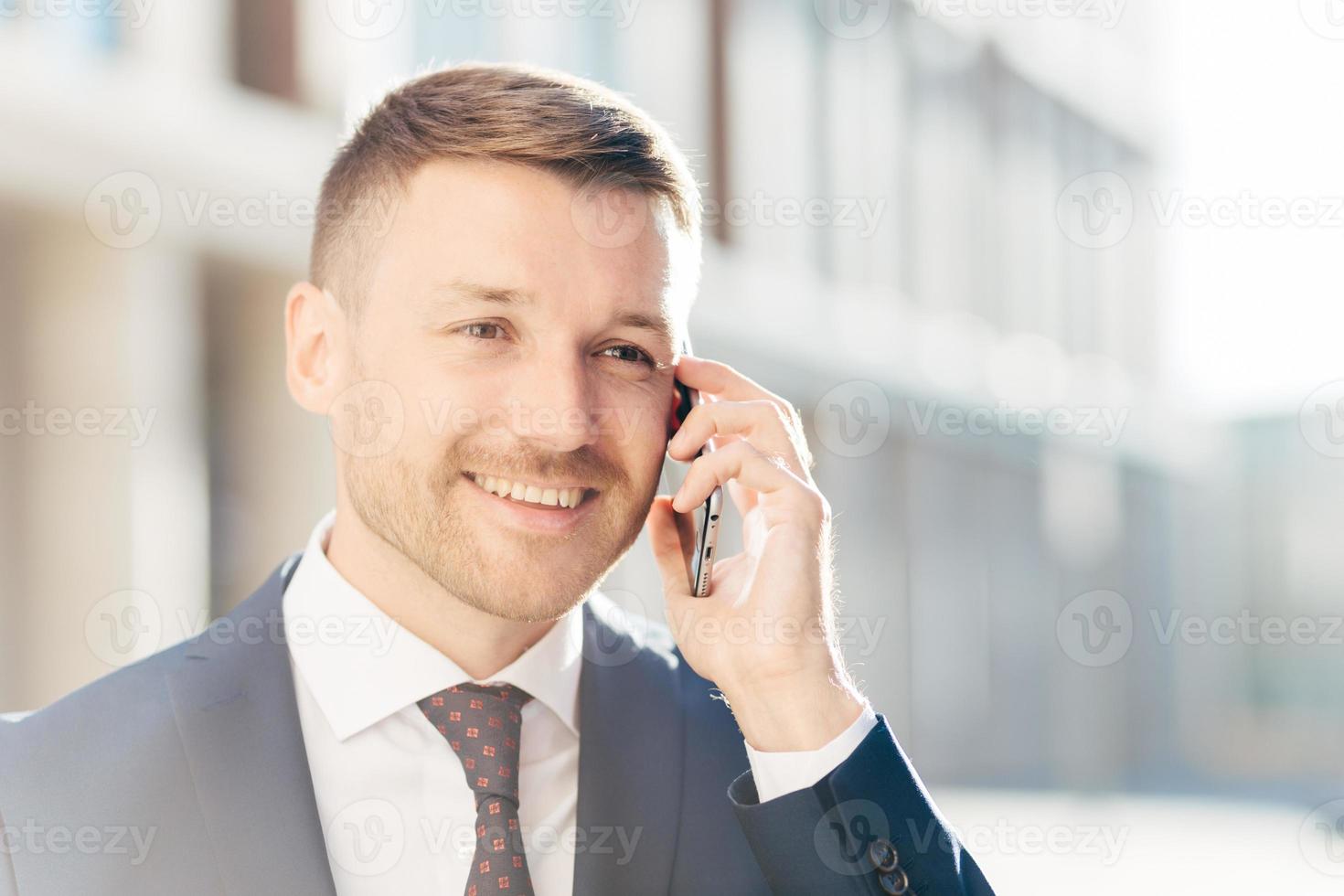 empresário de meia-idade feliz confiante se comunica via celular, discute o relatório financeiro com o parceiro de negócios, usa roupas formais, fica ao ar livre contra um fundo desfocado. CEO ocupado foto