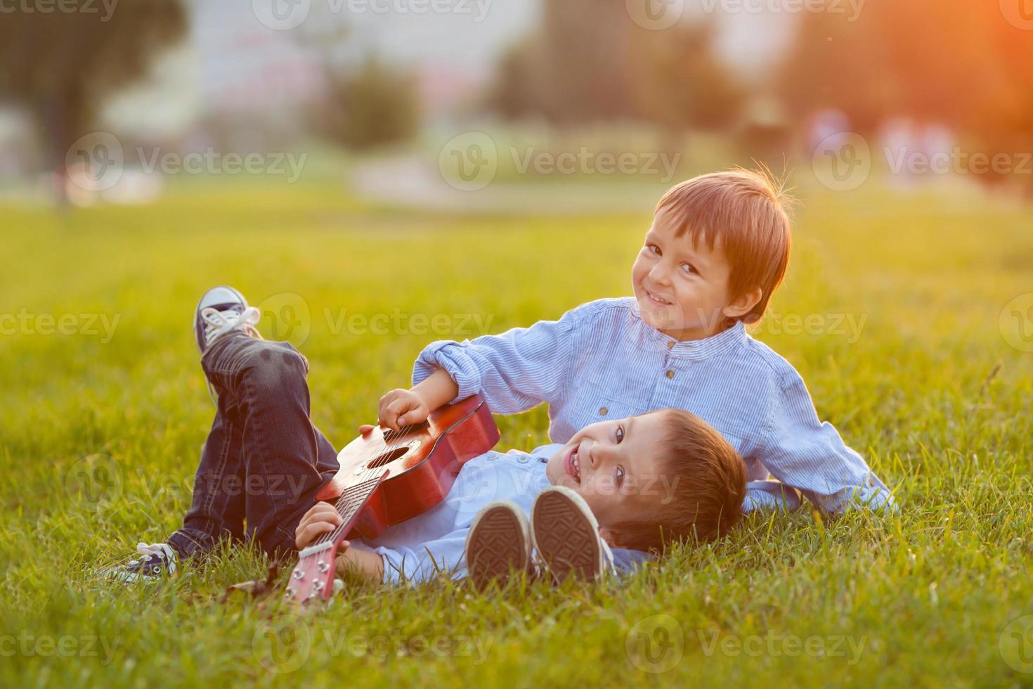 dois meninos adoráveis, sentado na grama, tocando violão foto