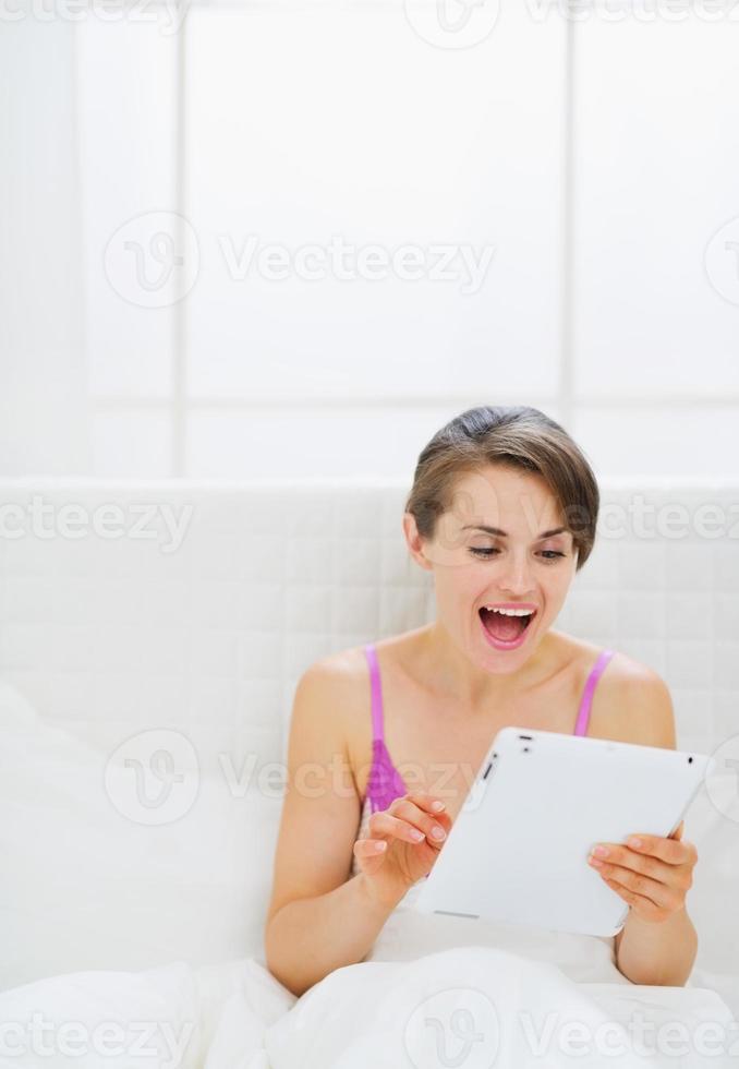 surpresa menina sentada na cama e usando o tablet pc foto