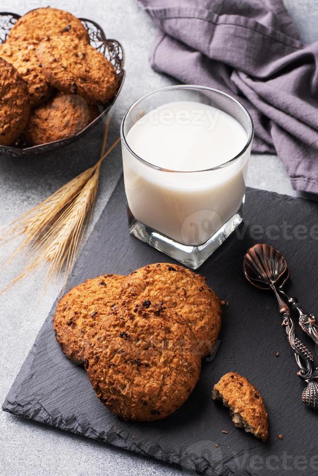 biscoitos caseiros cereais aveia e um copo de leite na mesa de concreto cinza. foto