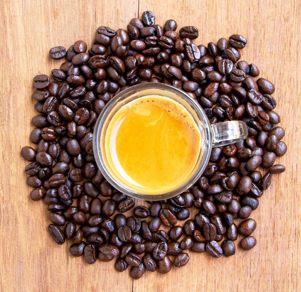 vista superior de uma xícara de café expresso quente com um bom creme em uma mesa de madeira cercada por uma pilha de grãos de café torrados marrons. foco seletivo na xícara de café foto