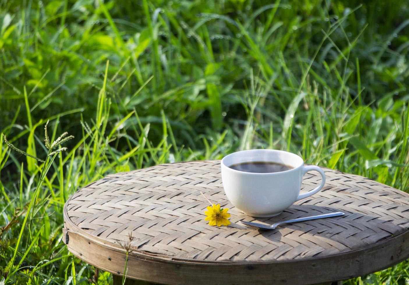 vista de alto ângulo de uma xícara de cerâmica branca de café americano preto em uma cesta de bambu com sol em fundo natural. conceito criativo de bebidas refrescantes de bom dia foto
