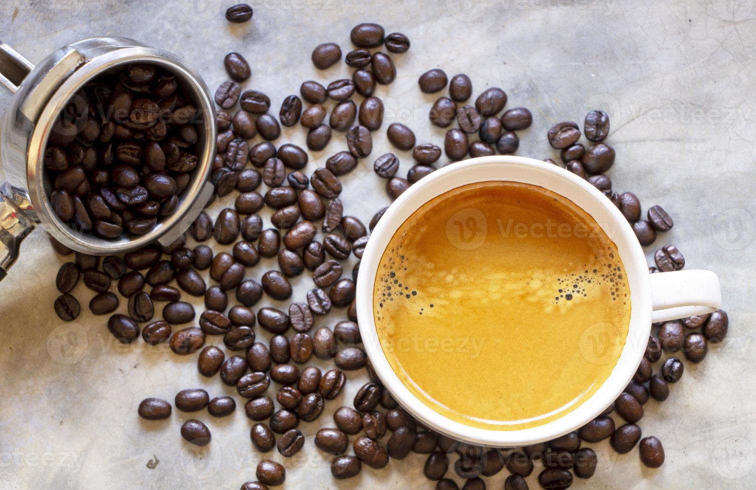 vista superior de uma xícara branca de café preto com uma pilha de grãos de café torrados orgânicos e suporte de filtro de café em uma mesa de concreto rústica foto