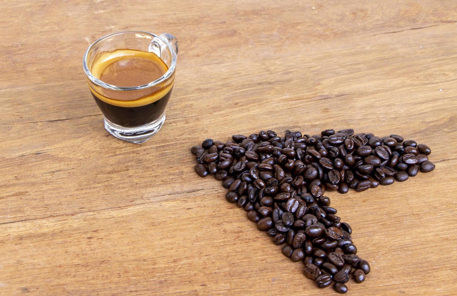 pilha de grãos de café marrom orgânico torrado com uma xícara de café expresso quente em uma mesa de madeira rústica de uma vista de alto ângulo foto