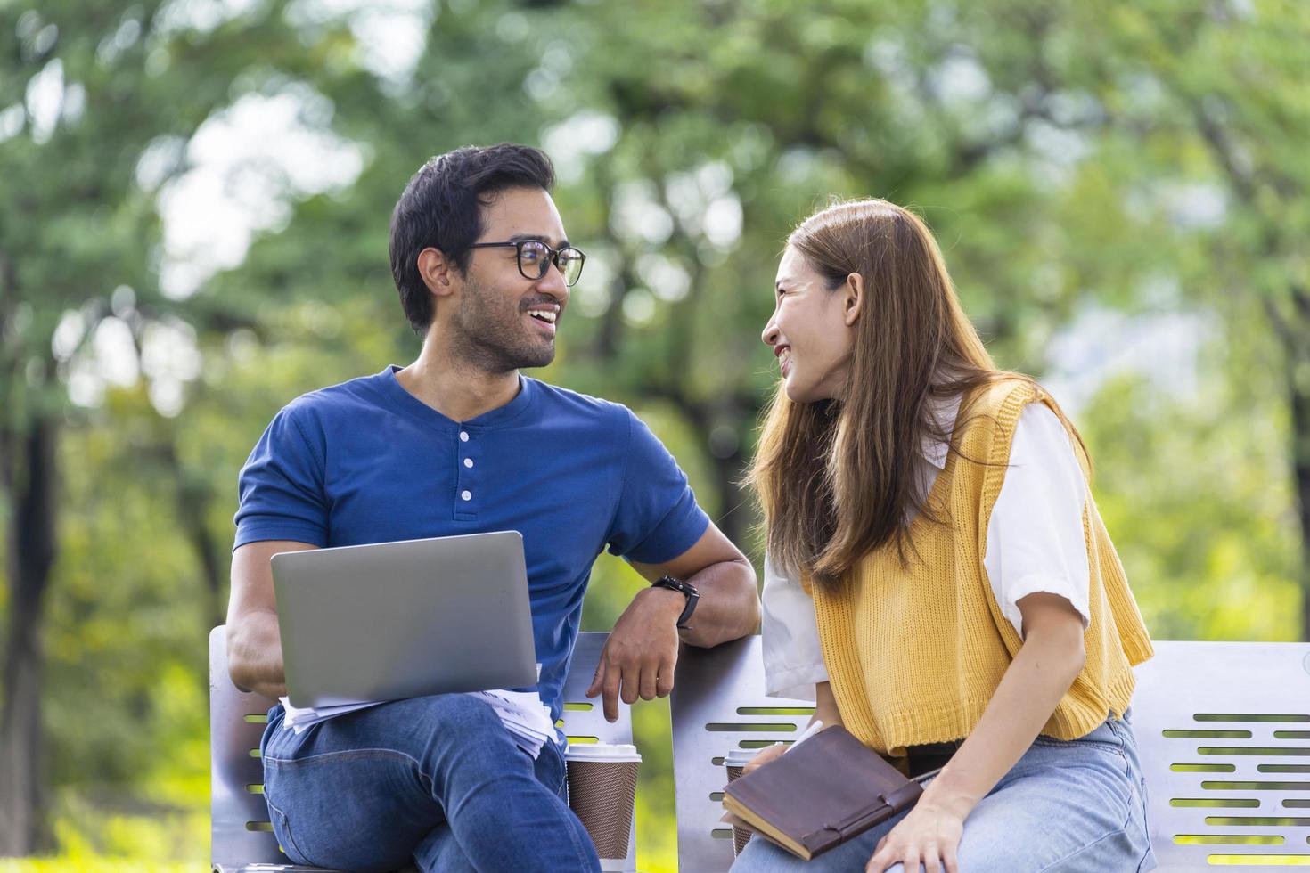 jovem casal asiático e indiano gosta de relaxar na chuva juntos no parque público enquanto se sentam juntos no banco durante o fim de semana foto