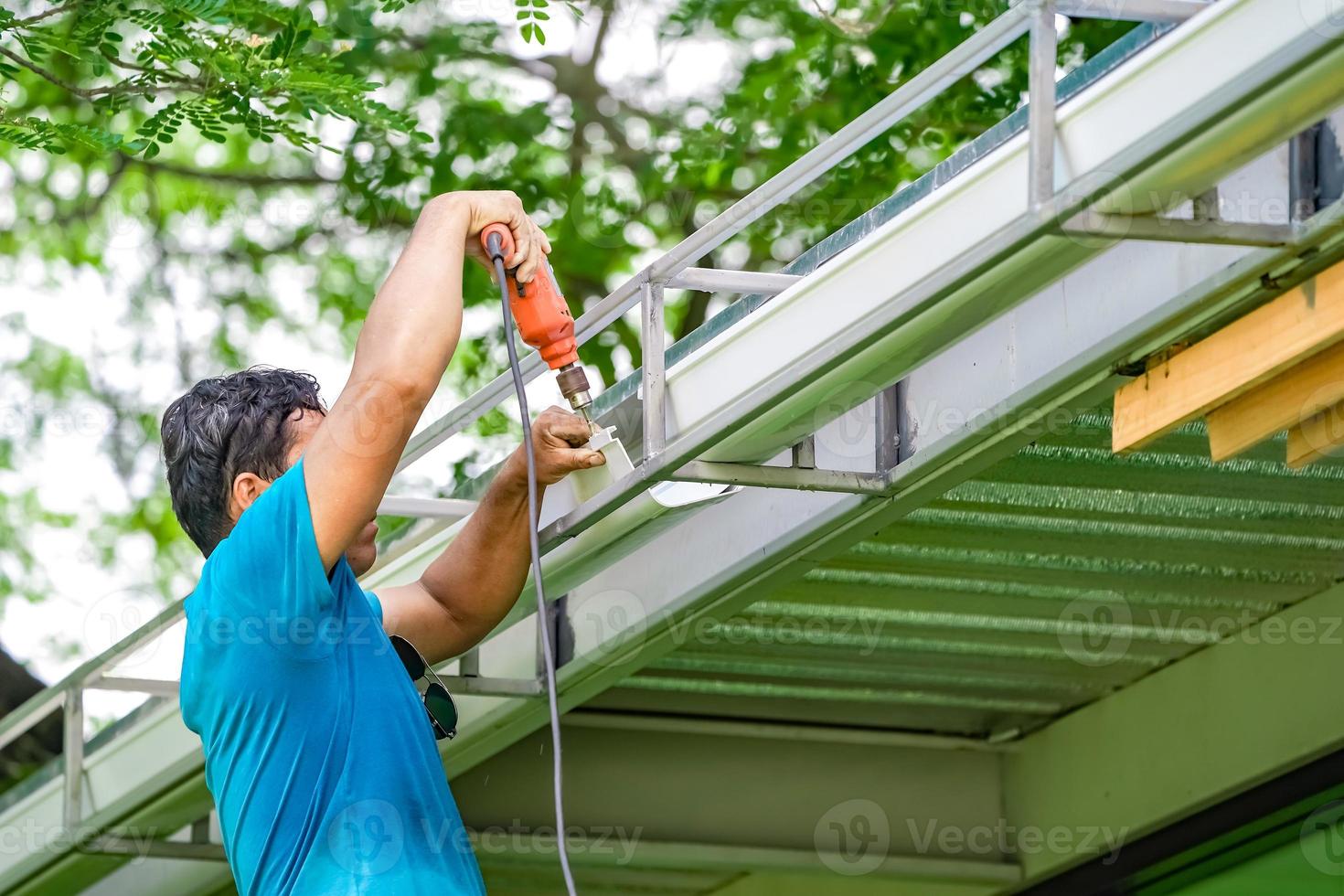 parafuso do trabalhador asiático, chave de fenda para criar e reparar o dreno de água do telhado. foto