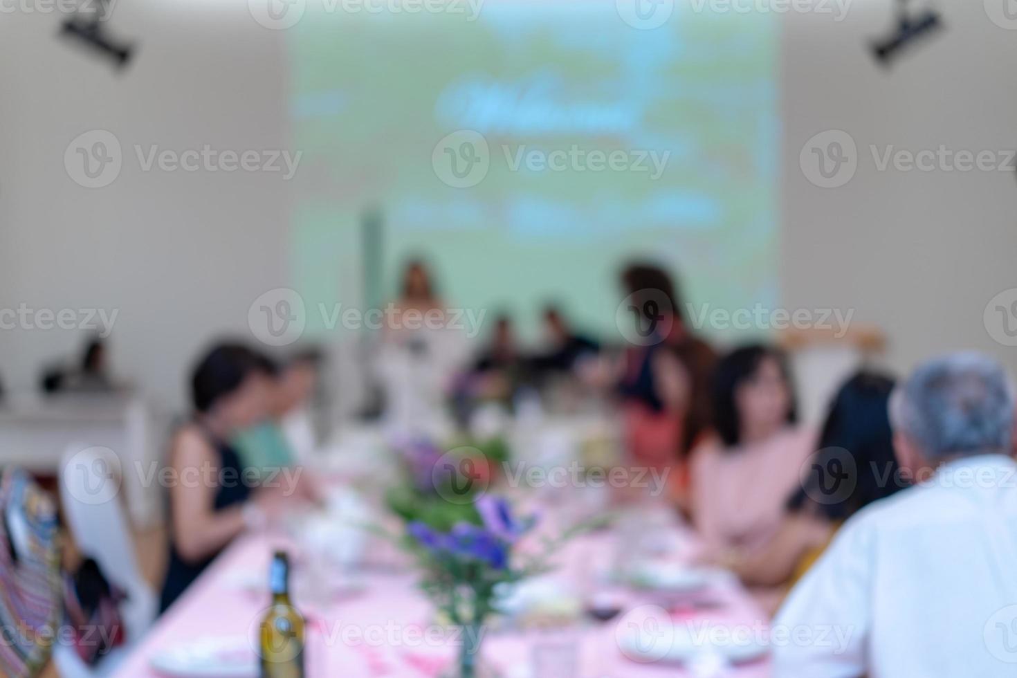 jantar embaçado com o projetor e tela branca para o público asiático sentado na longa fila da mesa. foto