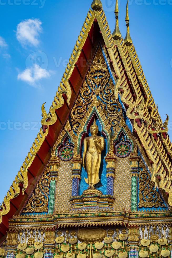 estátua de buda fica na frente do edifício do templo com belo estilo de padrão de arte tailandesa no dia de céu aberto. foto