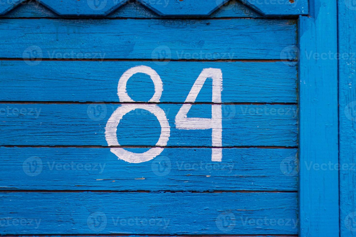 casa número 84. os números são pintados em tinta branca usando um estêncil em uma parede de madeira azul feita de tábuas velhas secas. a parede da casa da aldeia foto