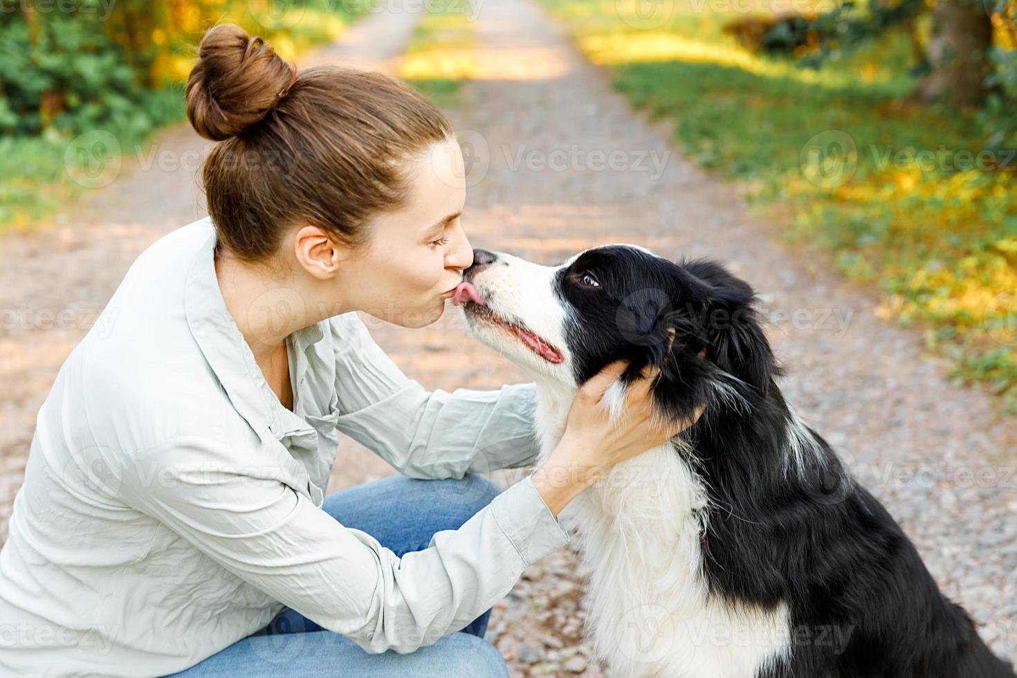 sorridente jovem atraente brincando com border collie cachorrinho fofo no fundo ao ar livre de verão. menina segurando abraçando amigo cão abraçando. conceito de cuidados e animais de estimação. foto