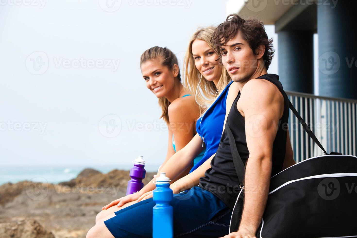 três jovens sorridentes com garrafas de água na praia foto