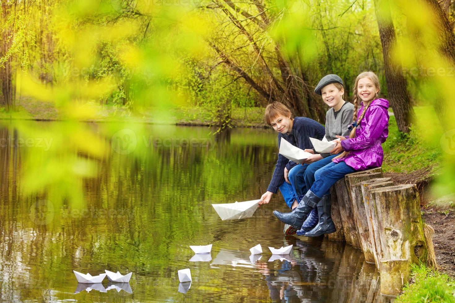 amigos sorridentes sentar colocando barquinhos de papel na lagoa foto