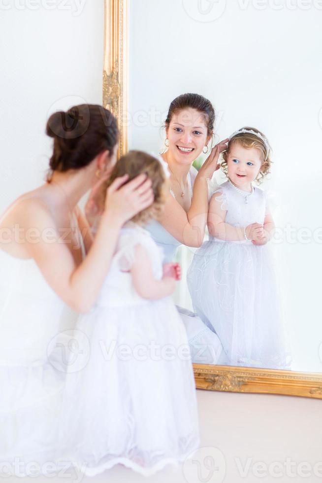 linda mãe e filha adorável criança experimentando vestidos brancos foto