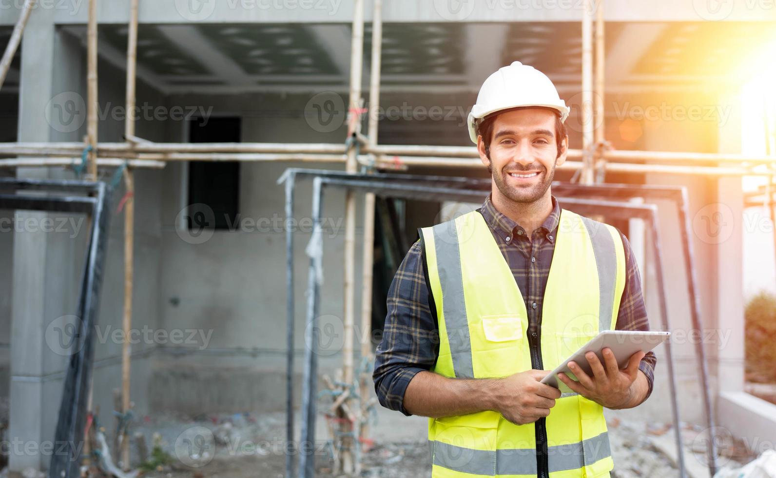 engenheiro civil masculino profissional ou arquiteto usa capacete de segurança. engenheiro, inspetor segurando tecnologia tablet para projeto de construção de lista de verificação no canteiro de obras. olhe para a câmera com cara de sorriso. foto