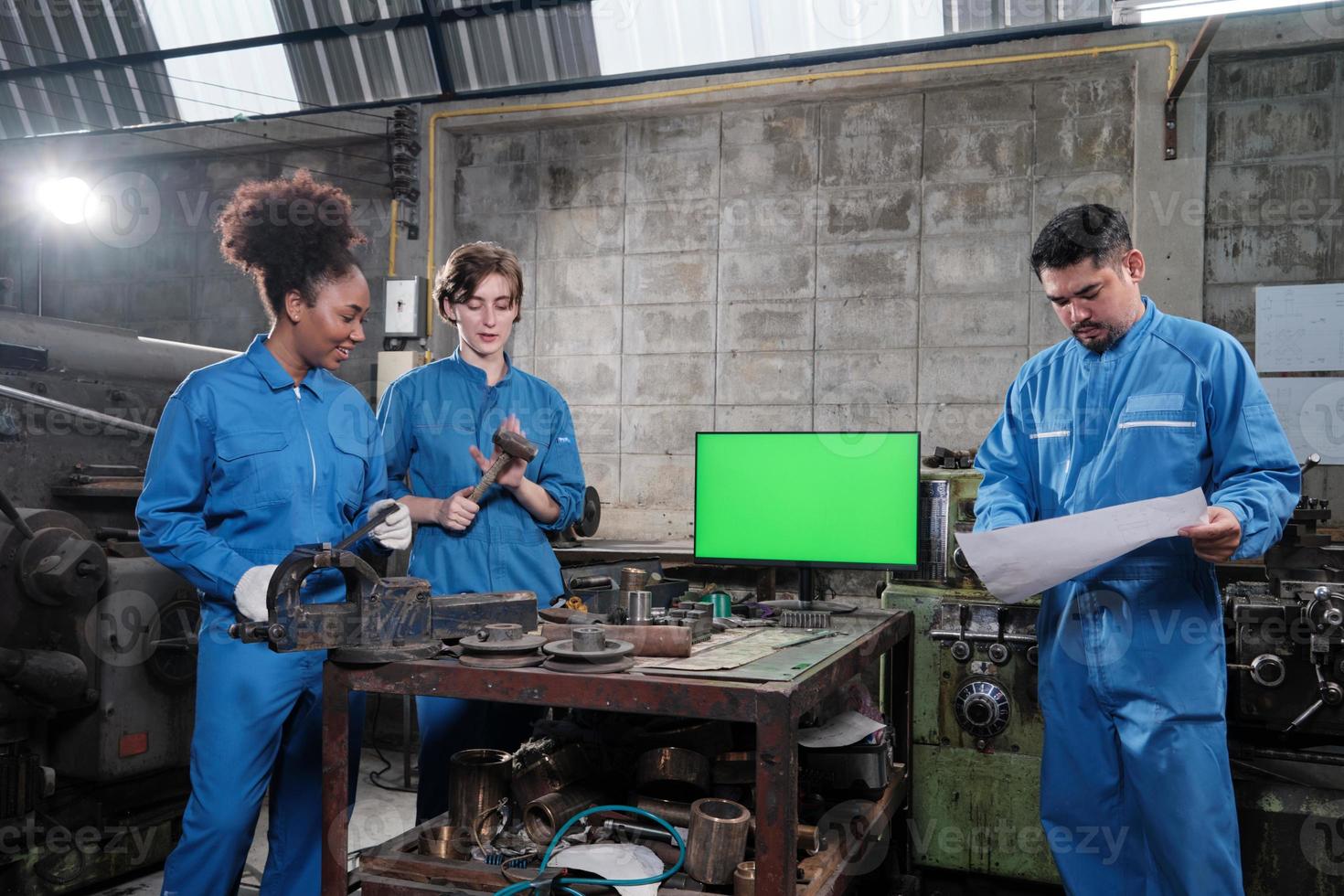 três equipes profissionais multirraciais de trabalhadores de engenheiros da indústria em trabalhos de metalurgia de uniformes de segurança discutem perto do monitor de tela verde, máquinas de torno mecânico e oficina na fábrica de fabricação. foto