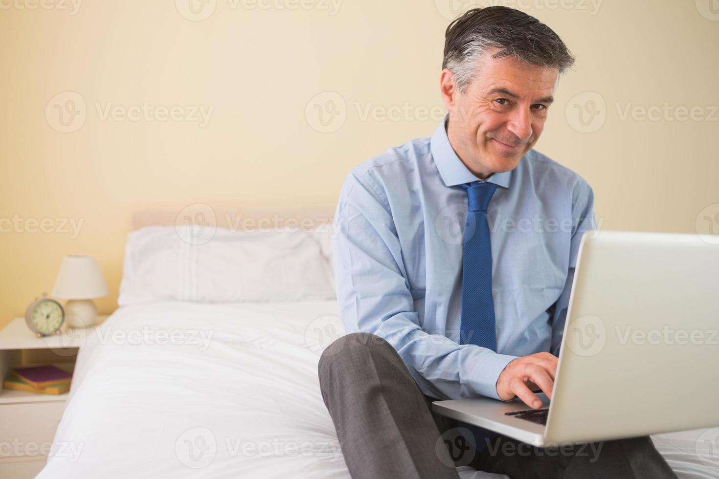 conteúdo homem usando seu laptop sentado em uma cama foto