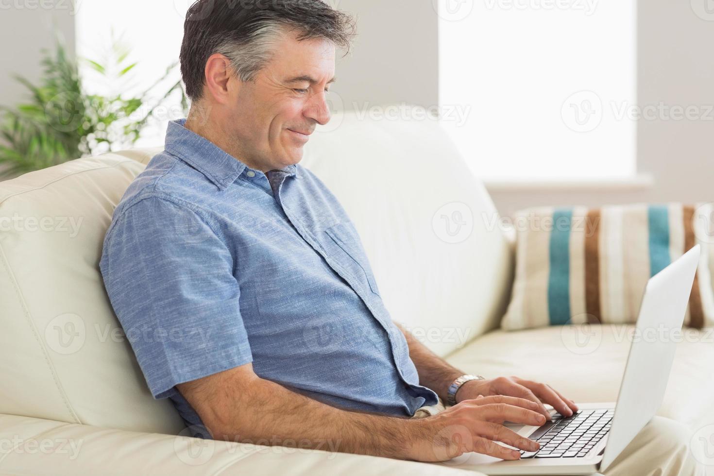 homem sorridente, sentado em um sofá usando laptop foto