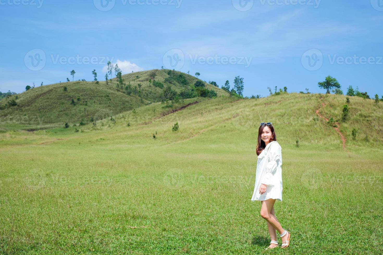 linda garota de pé e agindo na frente da montanha careca ou phu khao ya com campo de grama verde e céu azul. uma das atrações naturais de viagem na província de ranong, tailândia foto