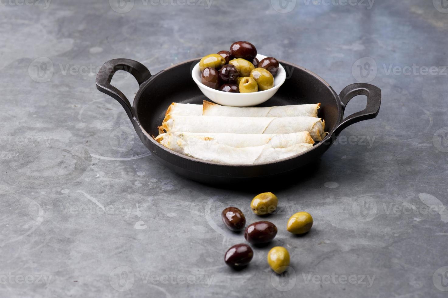prato de rolinhos de queijo com azeitonas, servido em uma panela preta foto