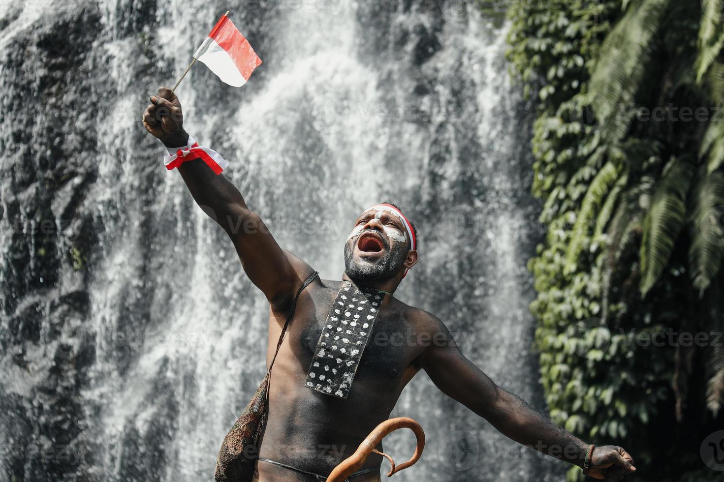 Papua homem da tribo dani diz merdeka, comemorando o dia da independência da indonésia contra o fundo da cachoeira. foto