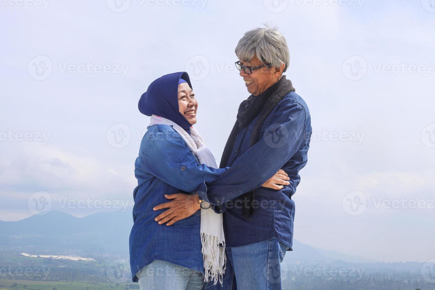 casal de idosos asiáticos. alegre bom casal romântico sênior é enfrentar um ao outro e sorrir contra a paisagem dramática. vista da plantação de chá, montanha e lago. foto